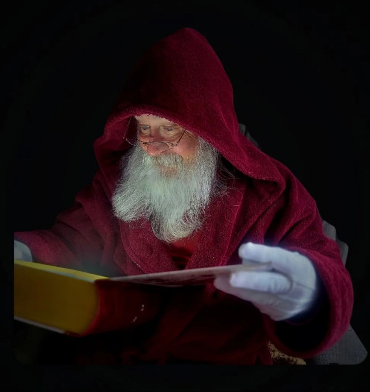 Elderly man in red robe reading a book.