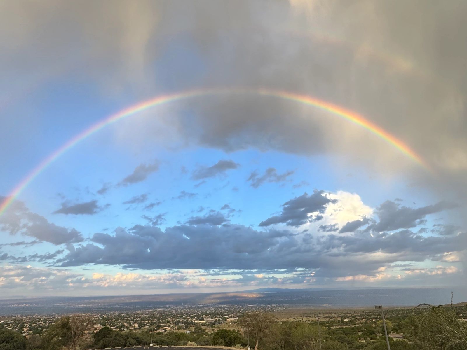 A vibrant rainbow arcs over a cityscape beneath a partly cloudy sky.