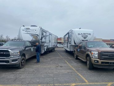 Two trucks towing large RV trailers in a parking lot under a cloudy sky.