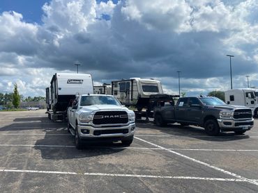 Two RAM trucks towing travel trailers under a cloudy sky in a parking lot.
