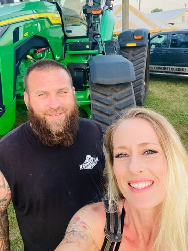 Smiling bearded man and woman posing in front of a green tractor.