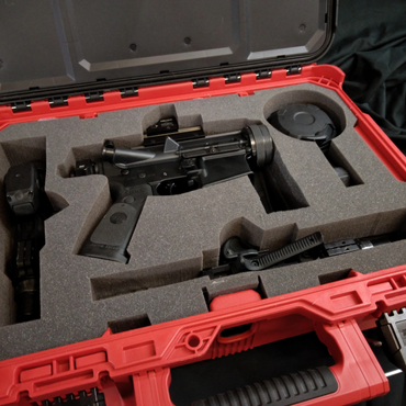 A black firearm partially disassembled in a red foam-lined case.