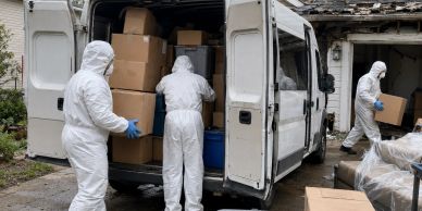 People in hazmat suits unloading boxes from a van.