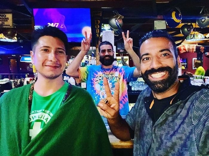 Three people, members of Psychedelic Club of San Mateo, smiling and making hand gestures at a bar.