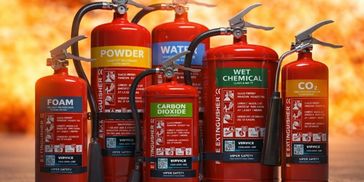 Different types of fire extinguishers in front of flames.