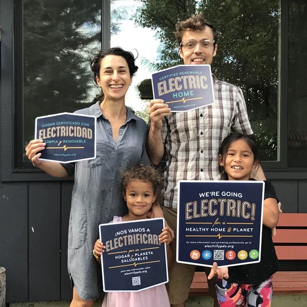 Family of four holding signs showing certified renewable electric home