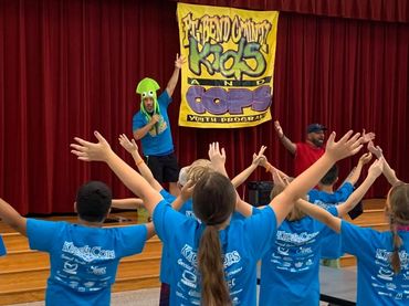 A group of kids with their hands raised in front of a stage.