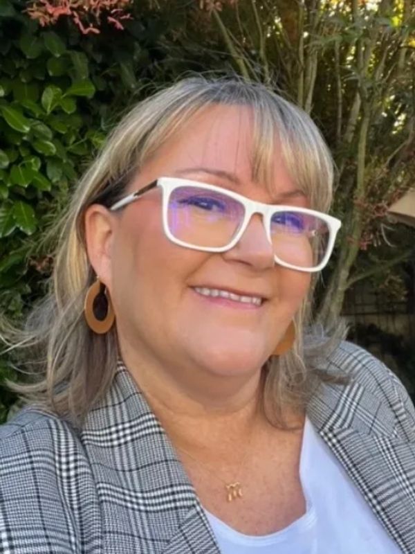Smiling woman with white glasses and checkered jacket.