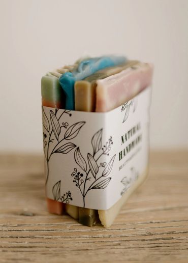 Colorful handmade natural soap bars wrapped in a botanical-themed label.