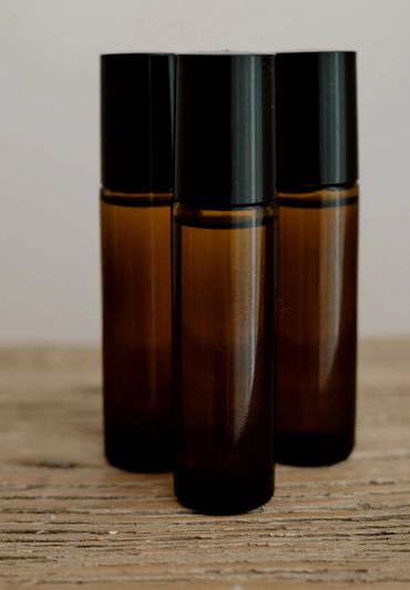 Three amber glass fragrance roller bottles with black caps on a wooden surface.