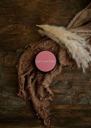 A container of Gulf Coast Soaps on a textured brown cloth with pampas grass accents.