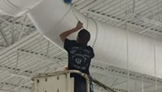 Professional cleaner on a scissor lift doing commercial high dusting inside a department store.