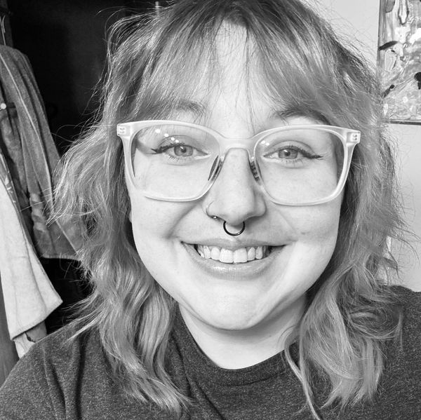 Smiling person with glasses and septum piercing in a black-and-white photo.