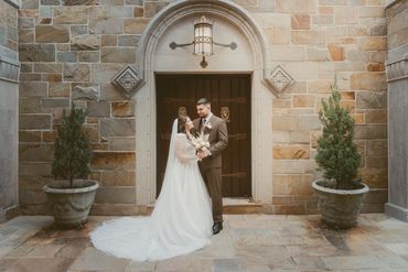 Bride and groom standing in front of a stone building, gazing at each other.