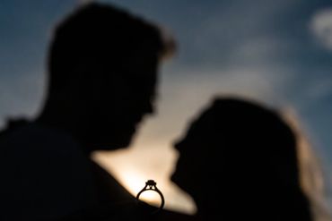 Silhouettes of a couple with an engagement ring at sunset.
