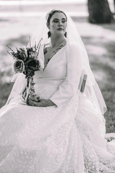 Black and white portrait of a bride in a detailed wedding dress holding a bouquet.