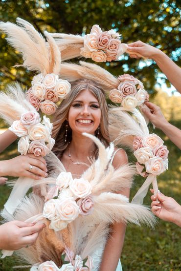 Smiling bride surrounded by pastel rose bouquets and pampas grass outdoors.