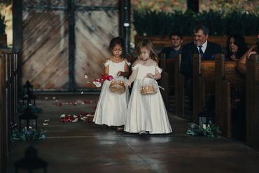 Two flower girls in white dresses walking down the aisle scattering petals.