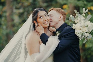 Bride and groom share a tender moment with a kiss and smile.
