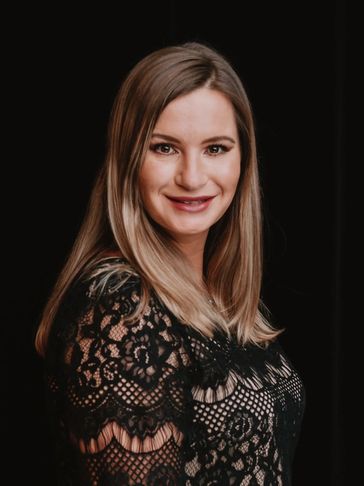 Smiling woman in a black lace dress against a dark background.