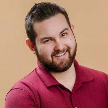 Smiling man with beard wearing a maroon polo shirt against a beige background.