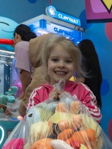 Little girl holding a bag of plushies she won at the Claw Vault