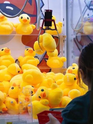 Child playing claw machine filled with yellow ducks.