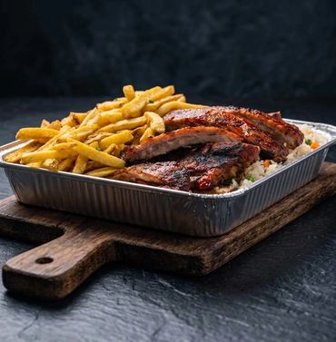 Charcoal-grilled BBQ ribs served in a foil tray over yellow rice and fresh-cut fries at Long Ave BBQ