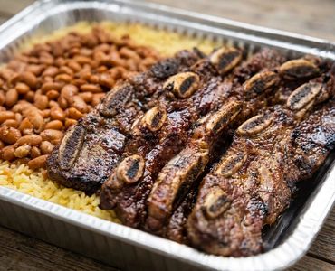 Charcoal-grilled BBQ short ribs tray served with seasoned yellow rice and beans at Long Ave BBQ