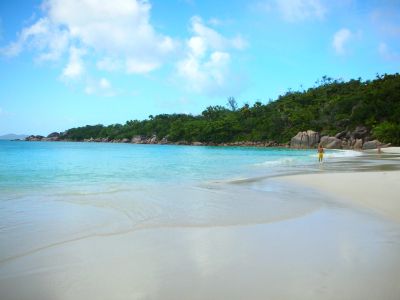 A peaceful beach with clear blue water and a person walking along the shore.