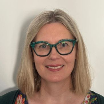 Smiling woman with blonde hair and green glasses.