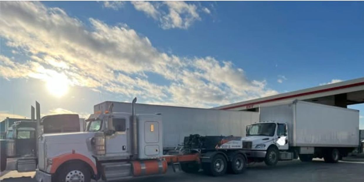 Two large trucks parked under a partly cloudy sky during sunset.