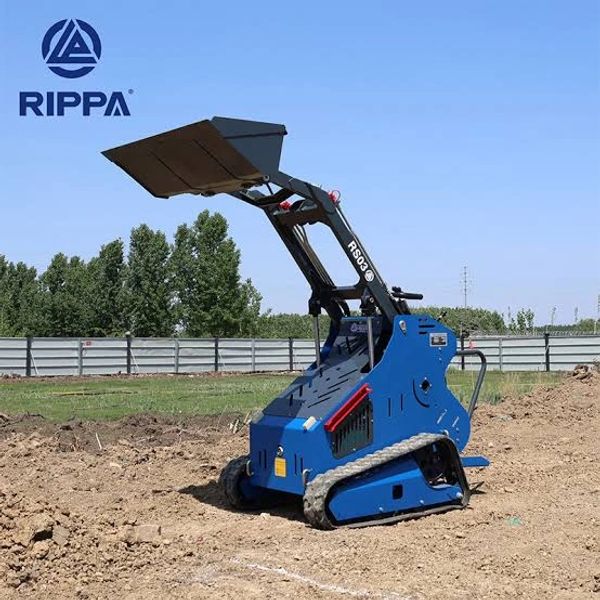 Blue mini loader with bucket attachment on dirt.