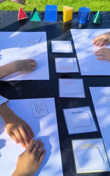 Mains d'enfants sur une table manipulant des cartes et du matériel de géométrie, cours collectifs.