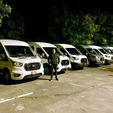 A person stands in front of a row of white vans at night.