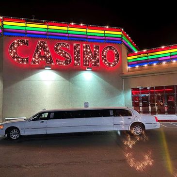 White limousine parked outside a brightly lit casino at night.