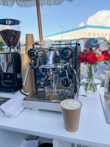 Espresso machine with coffee cup and fresh flowers on a white counter.
