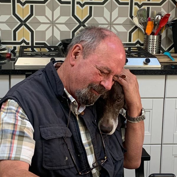 Man lovingly hugging his dog in the kitchen.