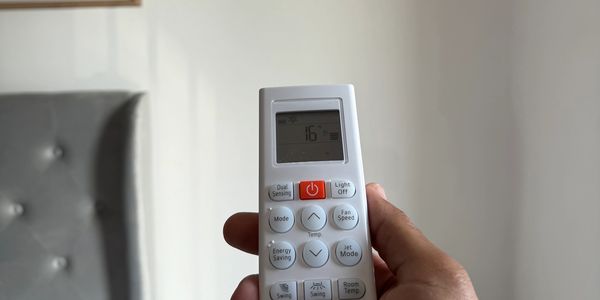 Hand holding a remote control for an air conditioner.