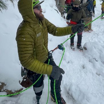 Man in green jacket climbing snowy terrain with rope.