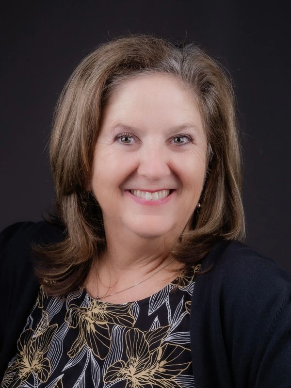 Smiling woman with shoulder-length hair in floral blouse.