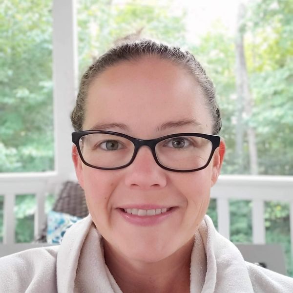 Woman with glasses smiling and sitting outside.