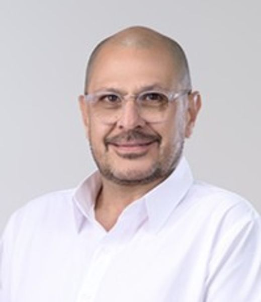 Smiling man with glasses wearing a white shirt against a light background.