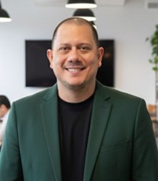Smiling man in a green blazer in an office setting.