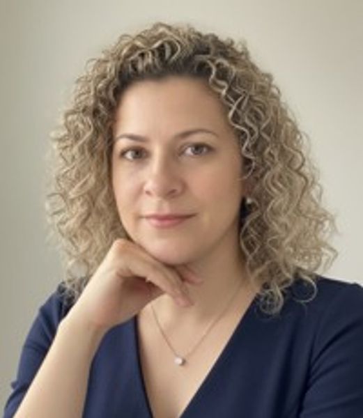 Woman with curly blond hair posing thoughtfully against a neutral background.