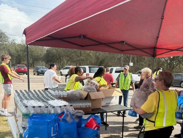 Volunteers distributing water and supplies under a red canopy.