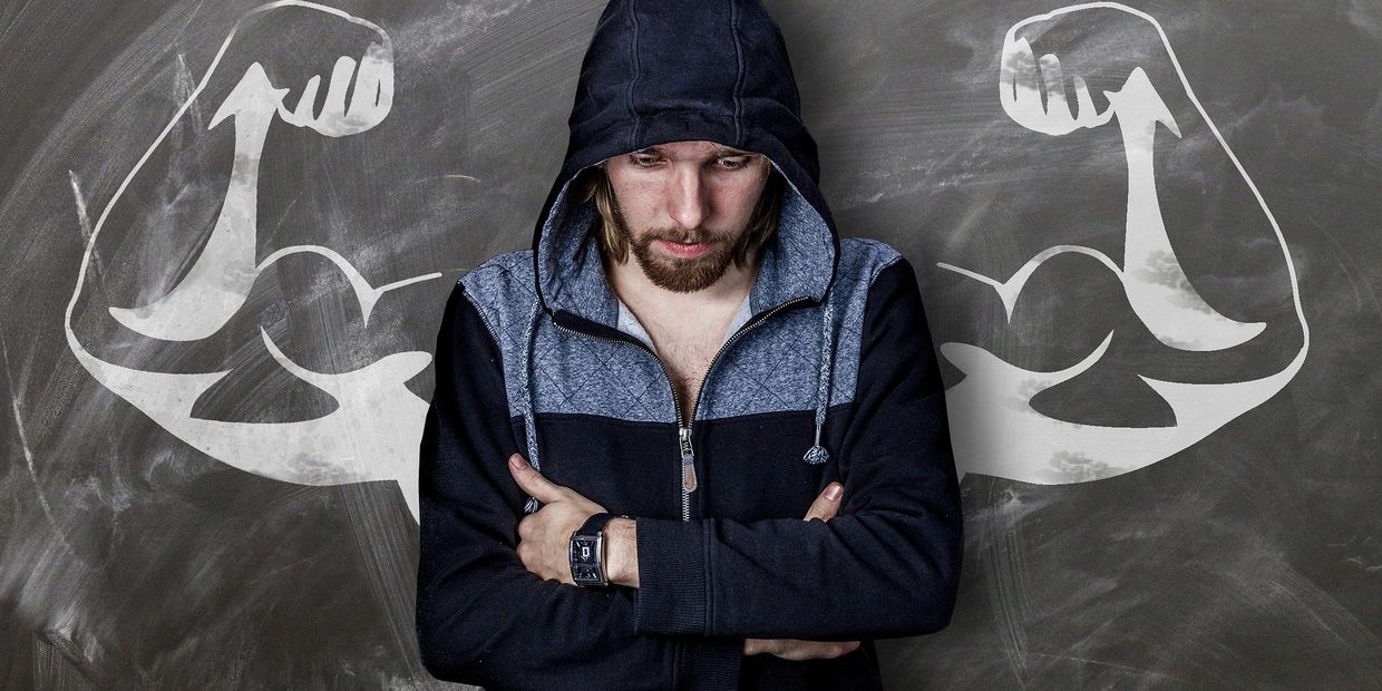 Picture of a young man, looking thoughtful, over a chalk image of strong arms behind him.