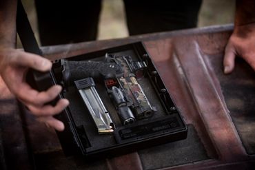 StopBox open on the table, with a pistol and a magazine visible, held open by hand.