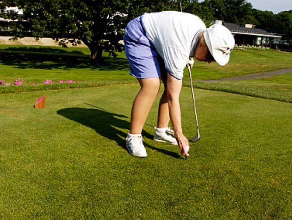 Senior age women bending to tee up a golf ball.