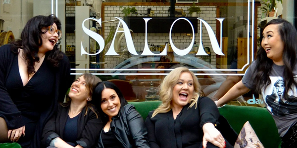 Five hair stylists sit on a green velvet couch on a sidewalk in front of Tarot Salon in downtown Boi